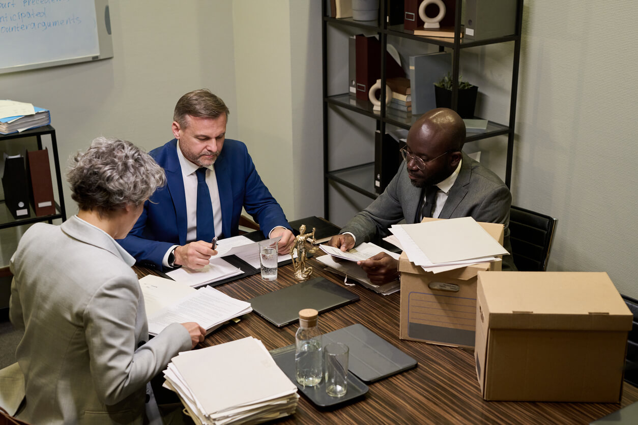 Three business litigation attorneys in Los Angeles reviewing corporate case documents over boxes of evidence.