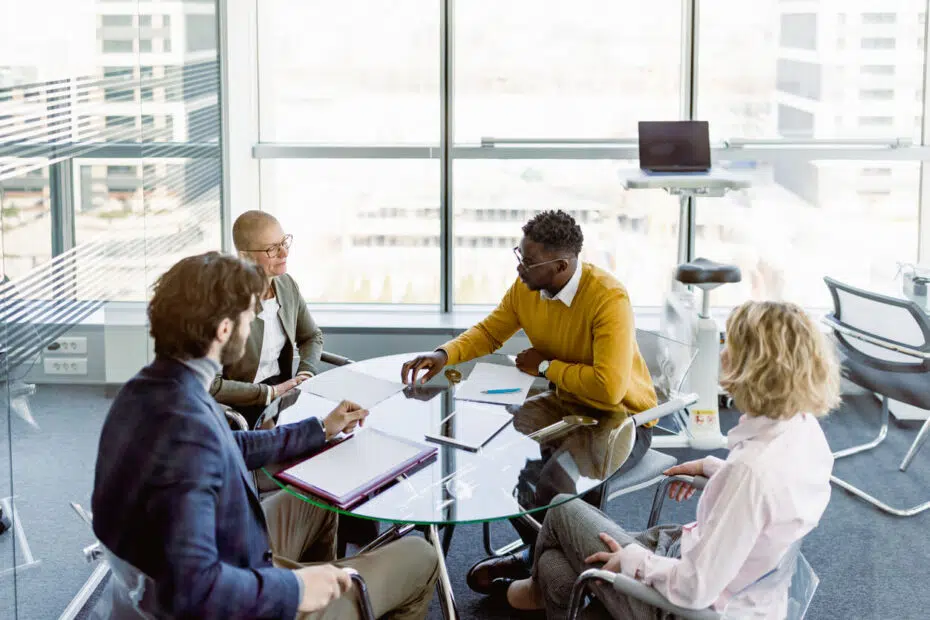 Corporate partners and investors reviewing legal contracts around a modern glass boardroom table during a business litigation dispute.